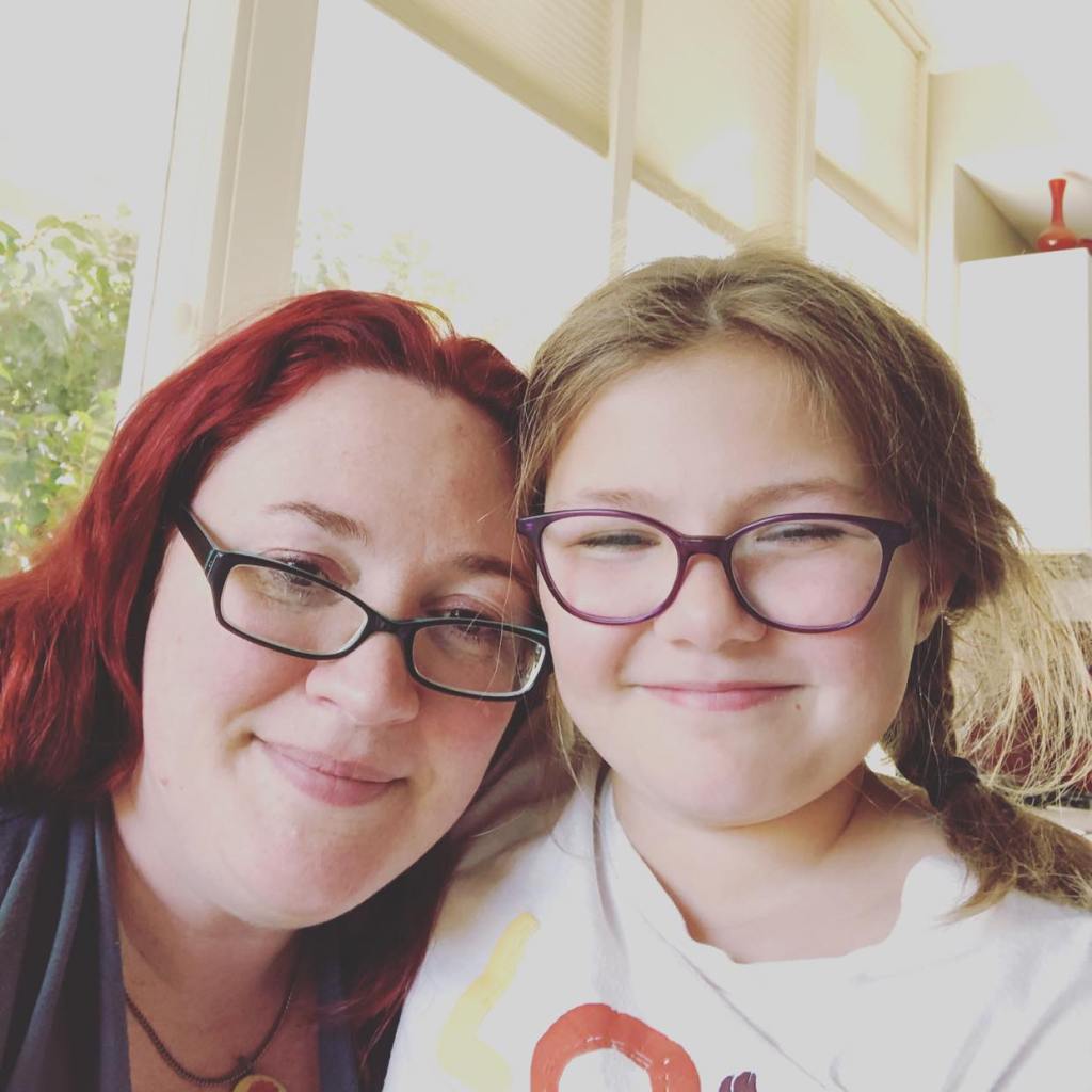 Mother and daughter, both wearing glasses, their arms around each other, smiling and crying into the camera.